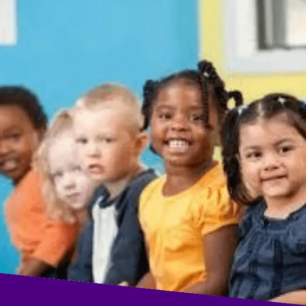 A group of diverse toddlers smiling and posing for a photo together at an indoor playground.